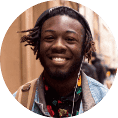 A young black man smiling at the camera with a colored top.